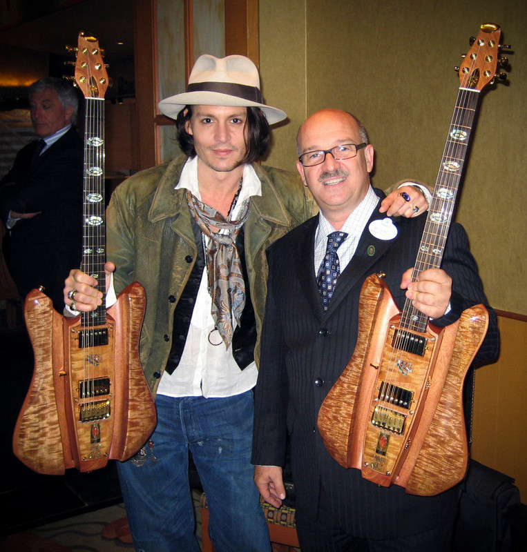 Two men pose indoors, each holding a figured-wood RKS guitar with an open body and gold hardware