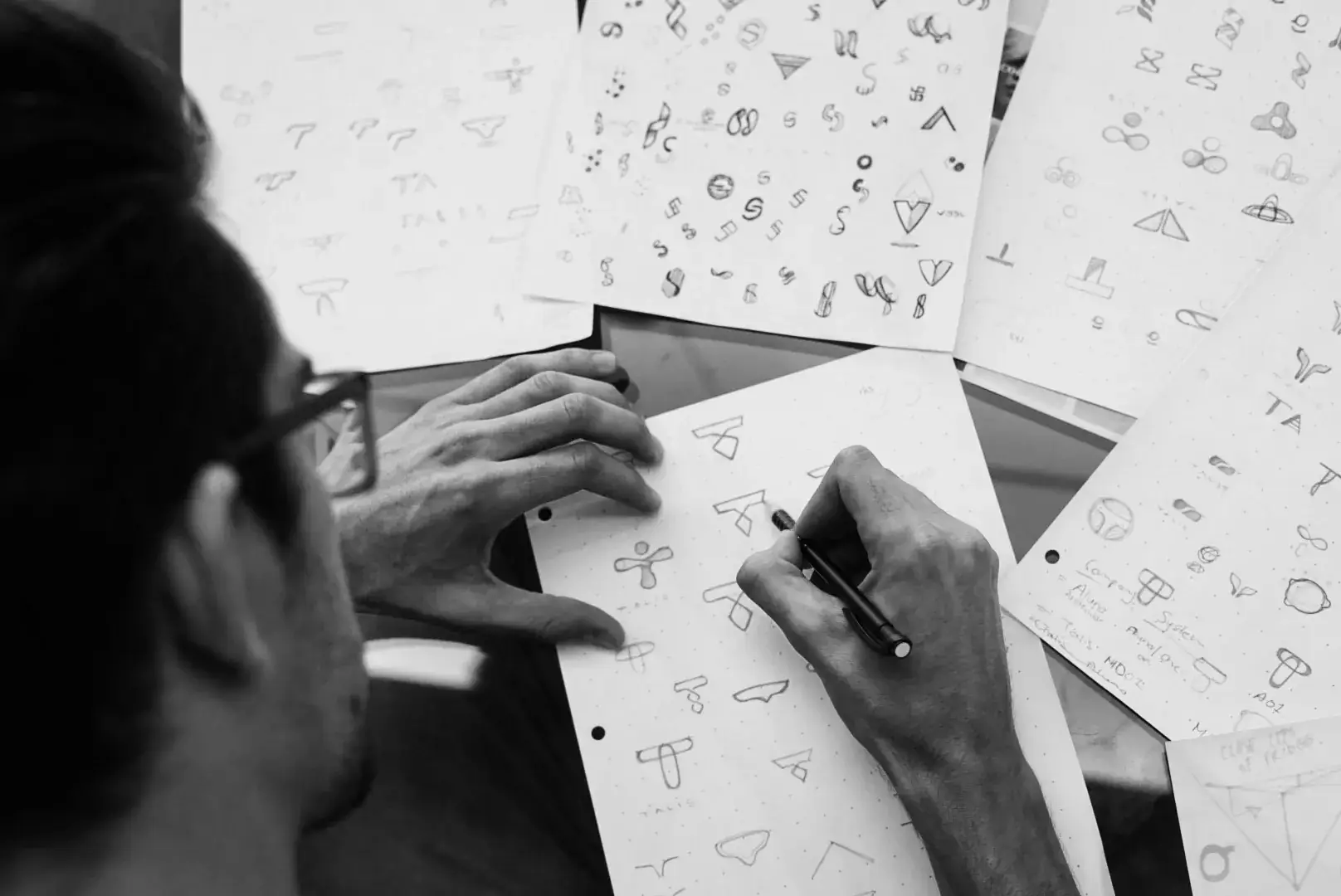 A designer sketching logo concepts in pencil across sheets of paper