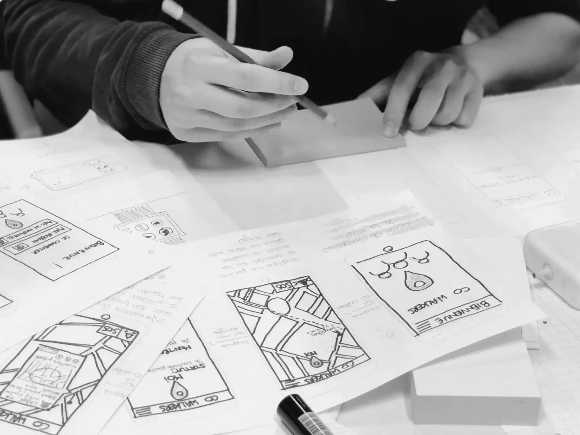 Hands sketching mobile app wireframe screens on paper