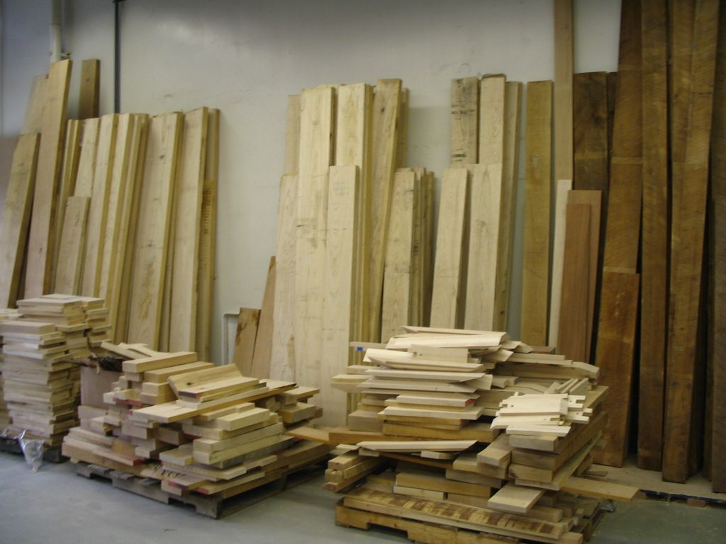 Rough-sawn wooden boards leaning against a white wall, with cut planks stacked on pallets in front