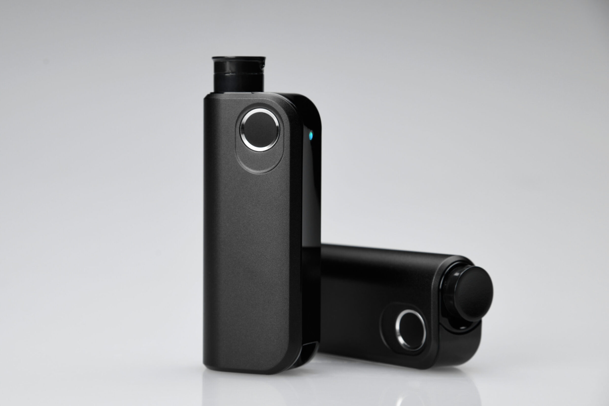 Two sleek, black electronic vaping devices are shown on a gray surface.
