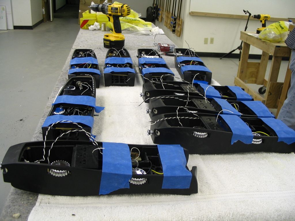 Black guitar body cores with exposed wiring and blue painter's tape laid out in rows on a padded workbench