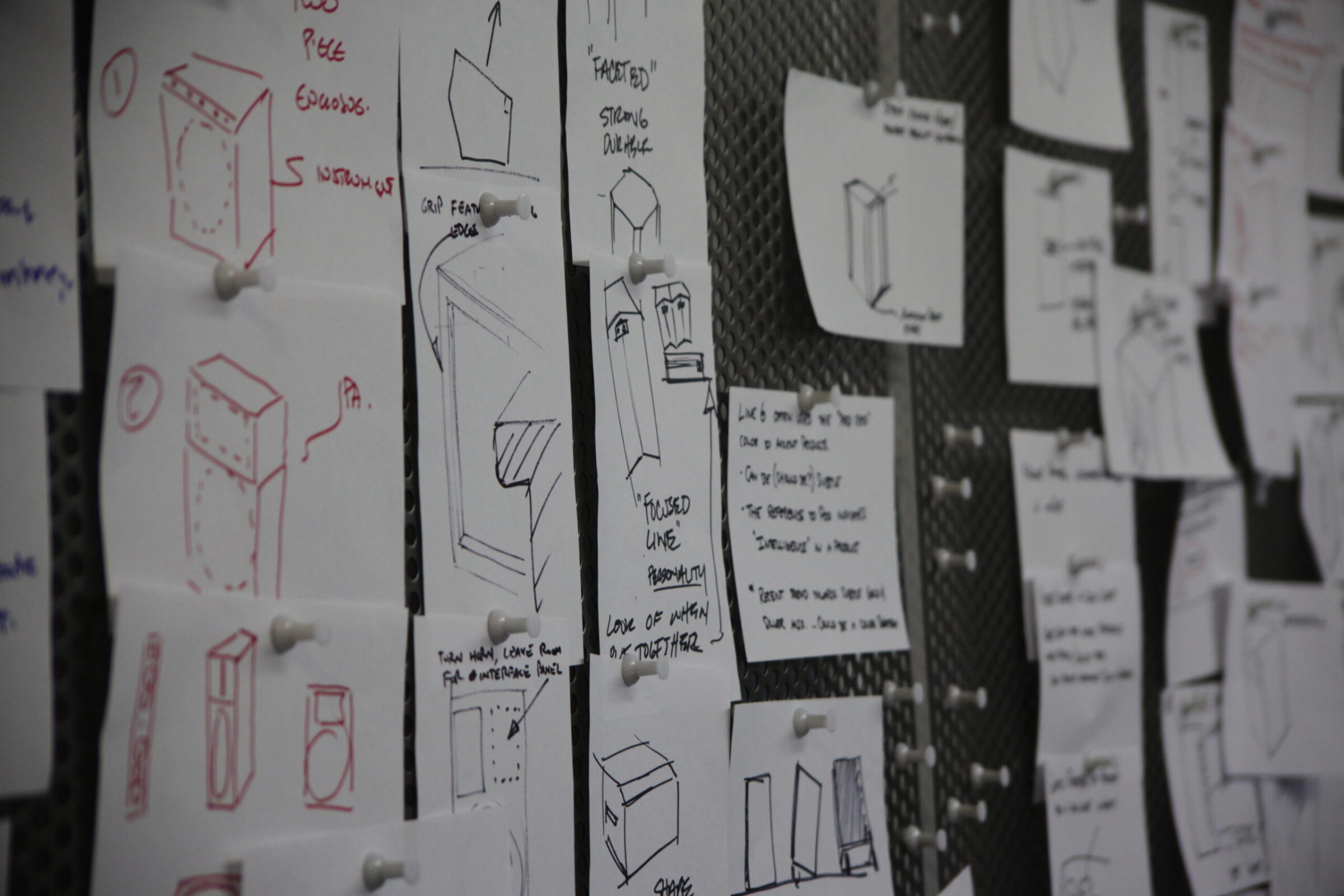 A bulletin board covered with sheets of paper displaying various hand-drawn sketches