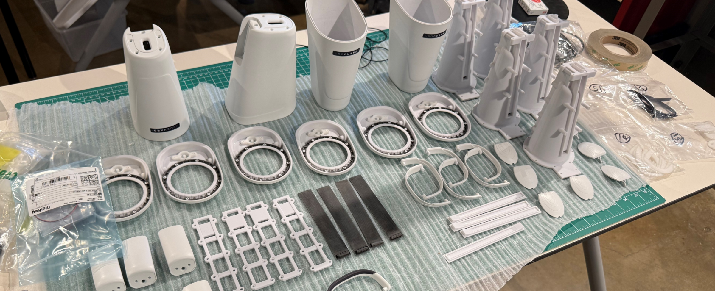 White prototype parts laid out on a cutting mat, including tapered housings, ring bearings, brackets and clips