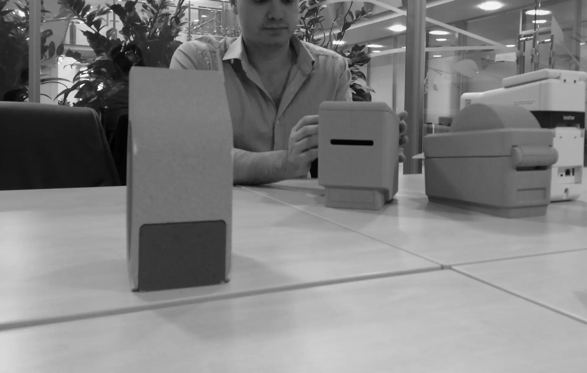 Black and white photo of a man at a table with three simple cardboard form models of a desktop printer