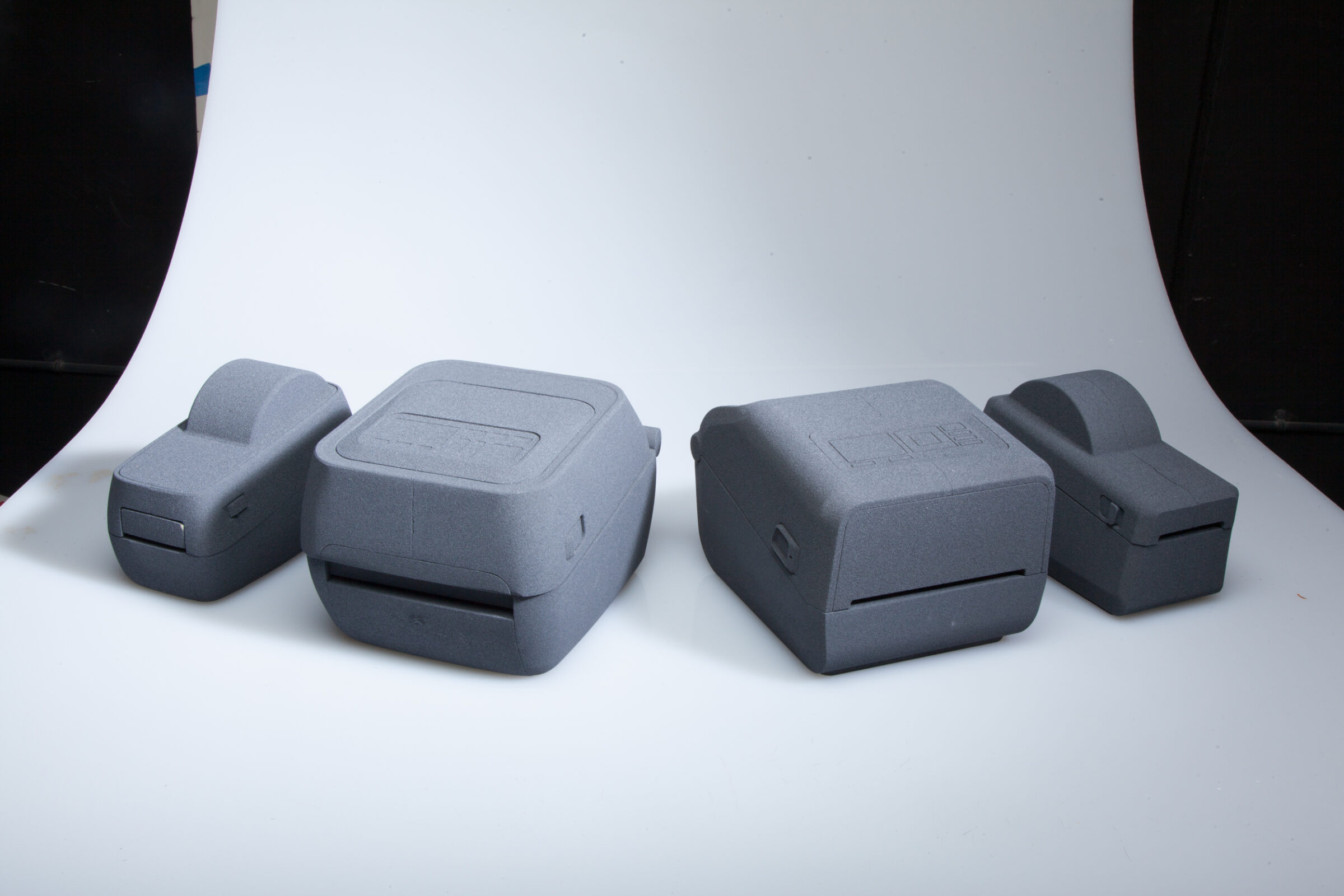 Four gray, rectangular devices with rounded edges are arranged in a row on a white curved surface.