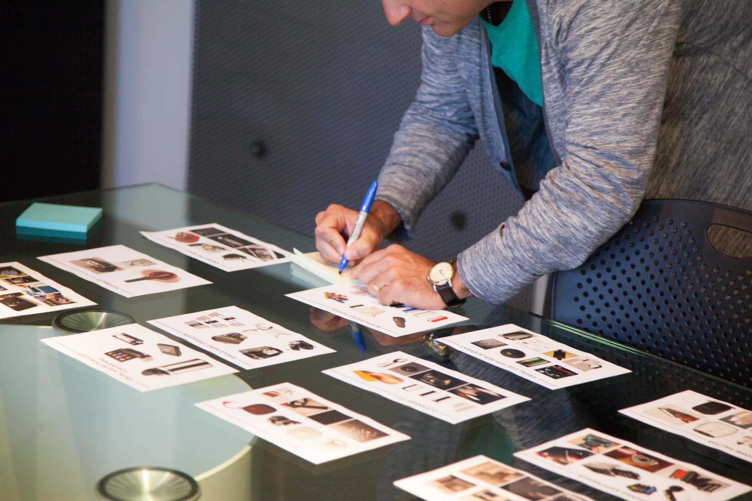 A man writes on cards of printed product images spread across a glass table