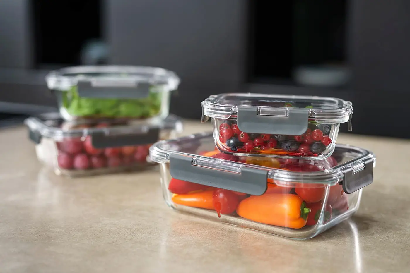 Three Zyliss containers filled with greens, berries and peppers on a kitchen counter.
