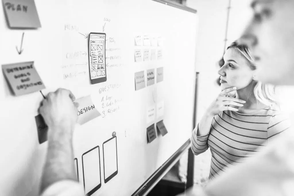 Two team members standing in front of a wall with notes and diagrams during a design meeting.