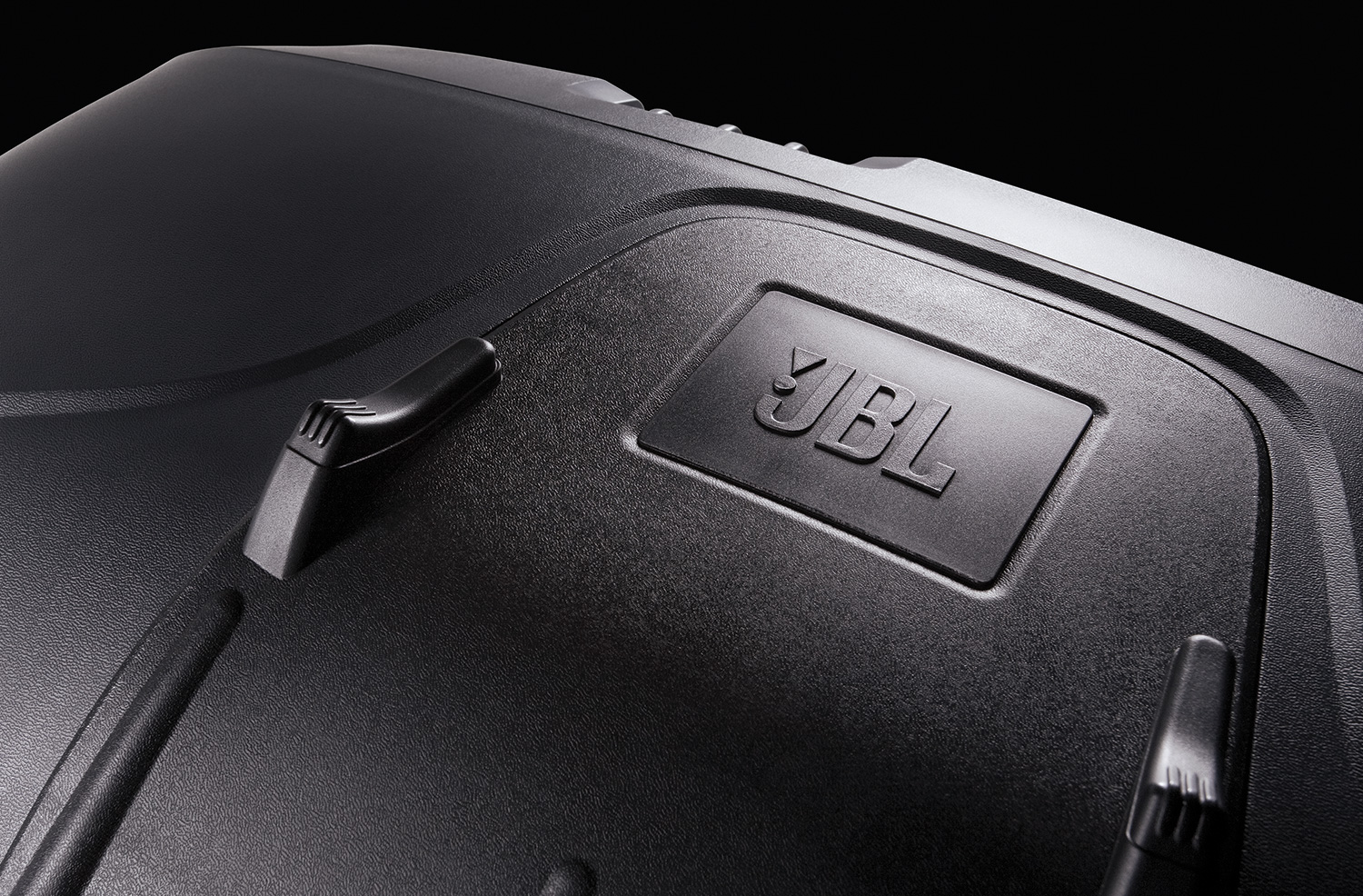 Close-up view of a black JBL speaker surface, showcasing the raised JBL logo and textured material—an example of sleek, modern contours that a top Product Design Firm or Design Consulting Firm might create under dramatic lighting.
