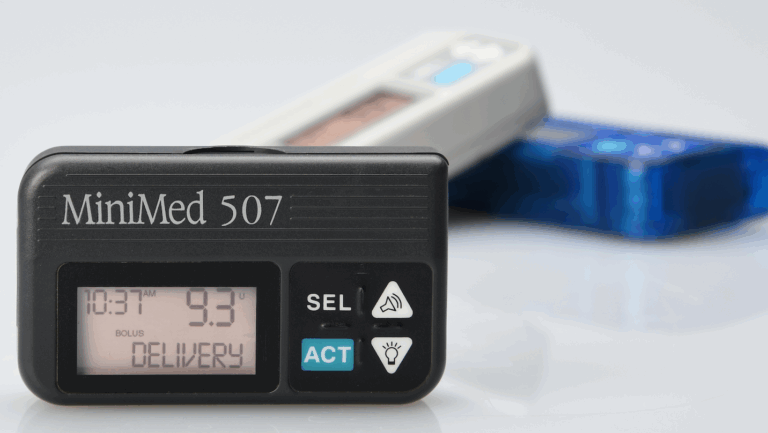 Front view of MiniMed 507 insulin pump displaying digital interface, with older models blurred in the background
