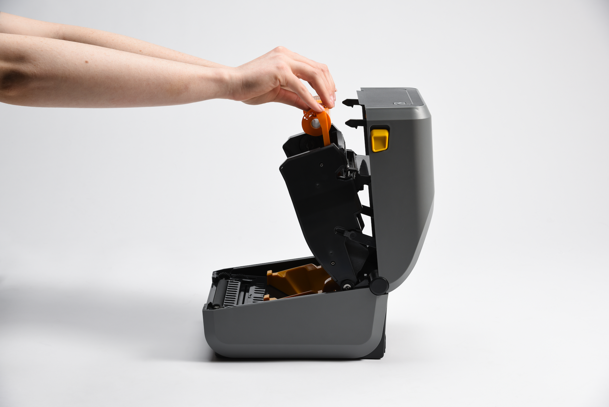 Hands inserting orange ribbon into Zebra printer during setup process