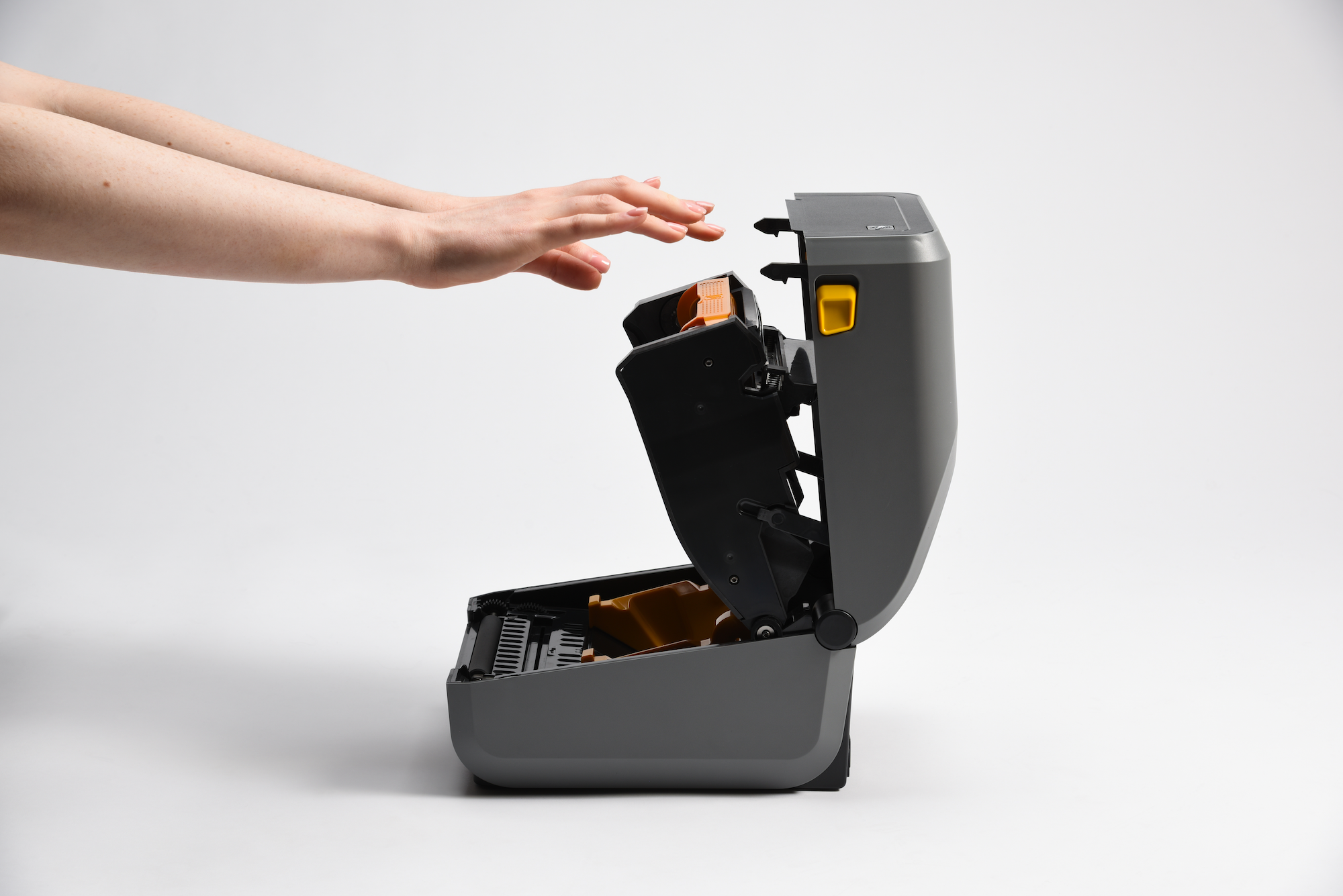 Hands reaching to press ribbon into Zebra printer, preparing for final closure