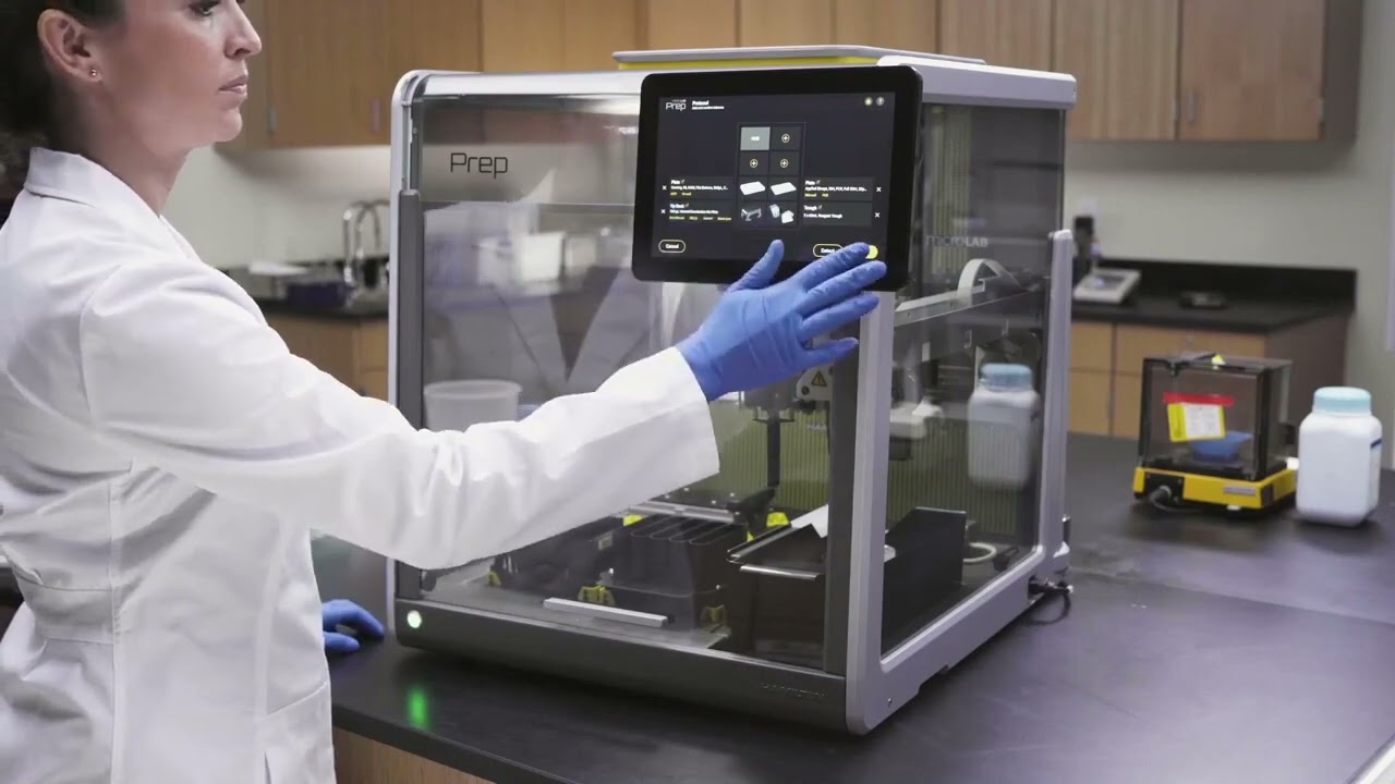 A scientist wearing a white lab coat and blue gloves operates a touchscreen interface on the AAA_Microlab automation machine inside a modern lab setting.