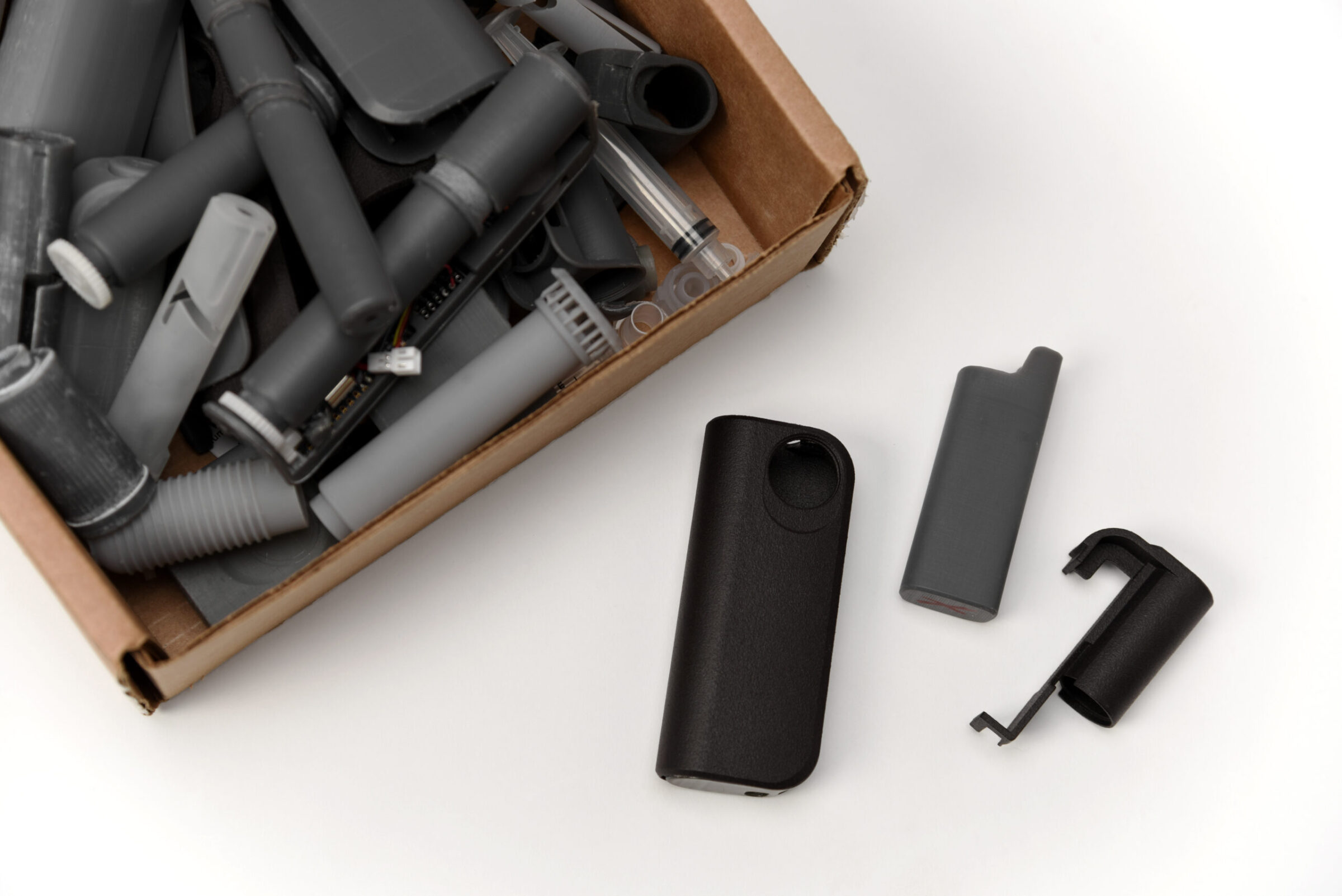 Box filled with assorted vacuum cleaner attachments on the left, with three black and gray plastic parts laid out on a white surface to the right of the box.