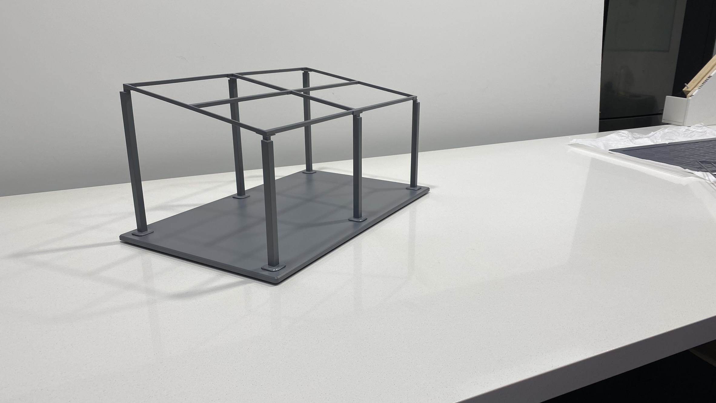 A small, gray, rectangular frame structure with vertical and horizontal bars sits on a white countertop in a well-lit room.