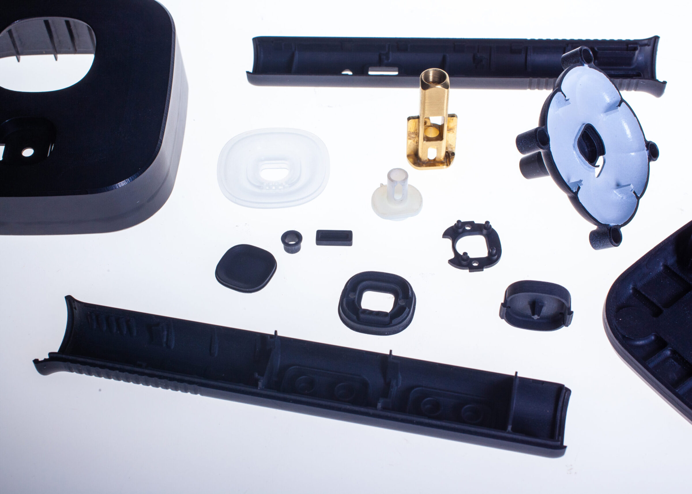 Assorted plastic and metal mechanical parts arranged on a white surface, including black covers, circular and rectangular components, and a gold cylindrical piece in the center—ideal for Perimetrics or InnerViewAI applications.