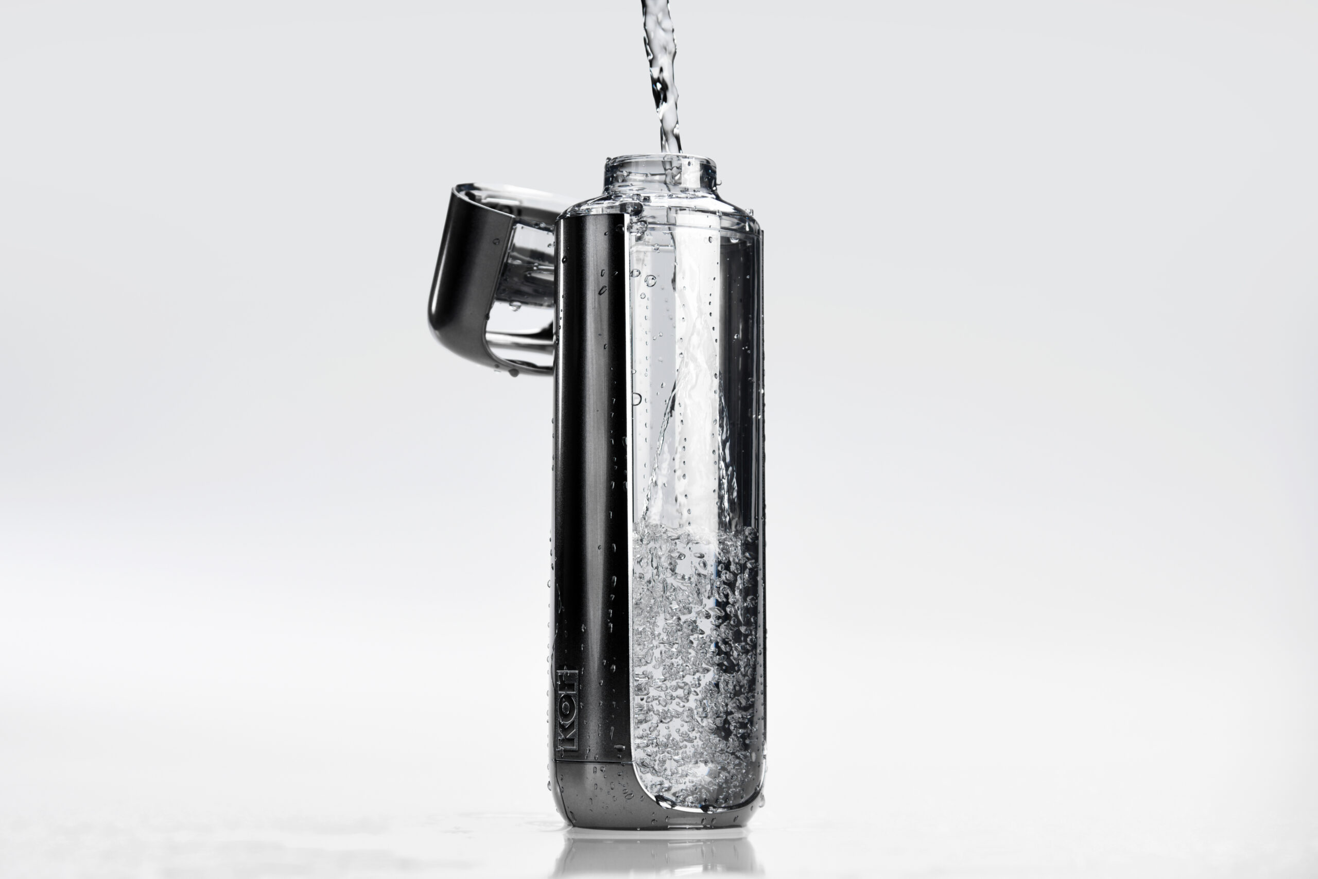 A clear, modern water bottle with a flip-top lid is being filled with water, shown against a plain white background. Bubbles are visible inside as the water pours in.