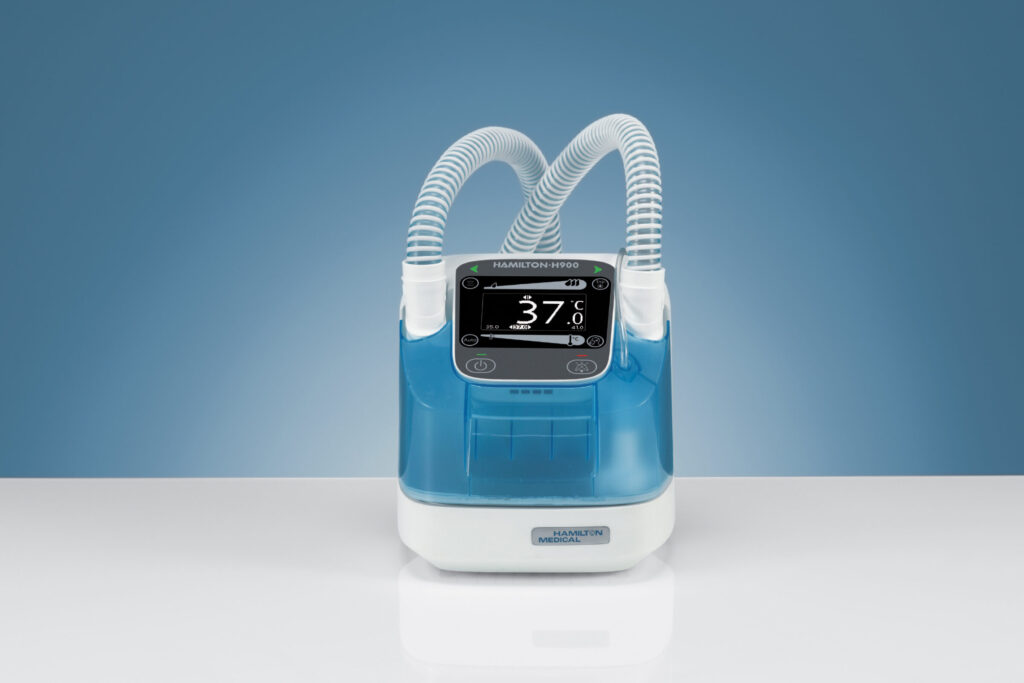 A blue and white medical device with two flexible tubes and a digital display showing a temperature of 37°C, placed on a white surface against a blue background.