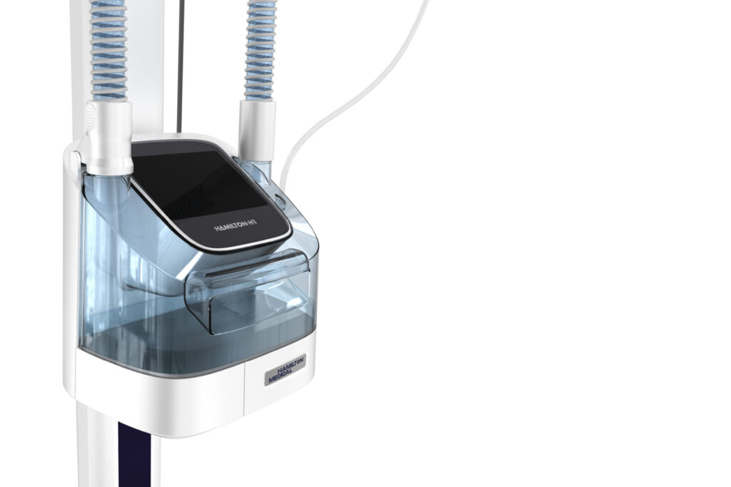 A close-up of a Hamilton Medical respiratory device with a transparent blue chamber, display screen, and two connected tubes, set against a white background.