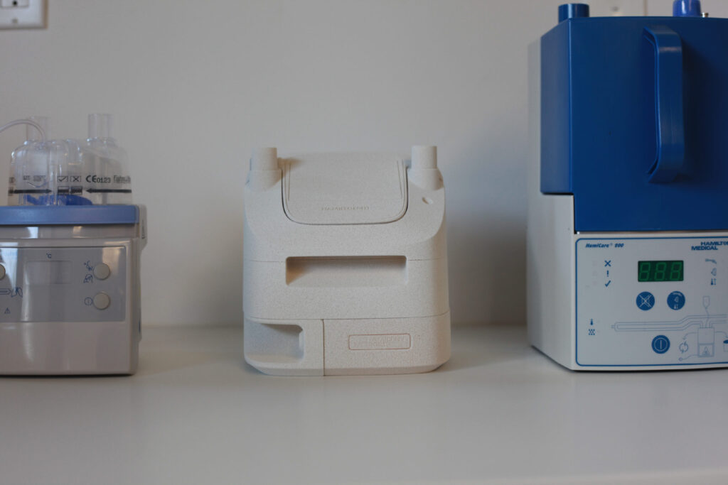 Three medical devices are placed side by side on a white counter; the one in the center is white and box-shaped, while the ones on the left and right have blue accents and control panels.